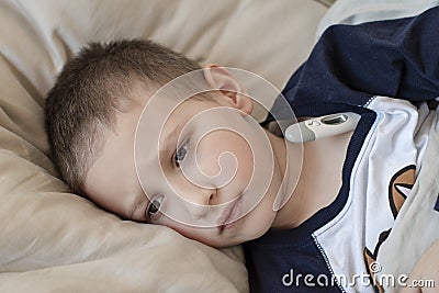 Pre-school sick boy in pyjama lying in bed with a digital thermometer Stock Photo